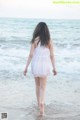 A woman in a white dress walking on the beach.