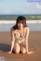 A woman in a white bikini sitting on a beach.