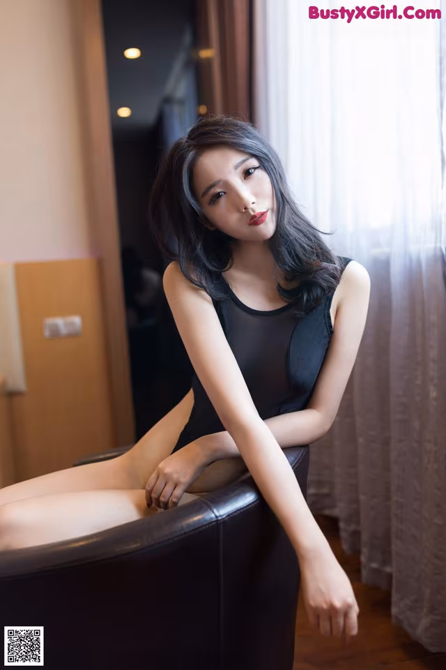 A woman in a black dress sitting on a black chair.