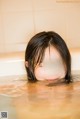 A woman in a bathtub with her eyes closed in the water.