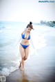 A woman in a blue bikini walking on the beach.