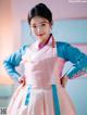 A woman in a pink and blue hanbok poses for a picture.