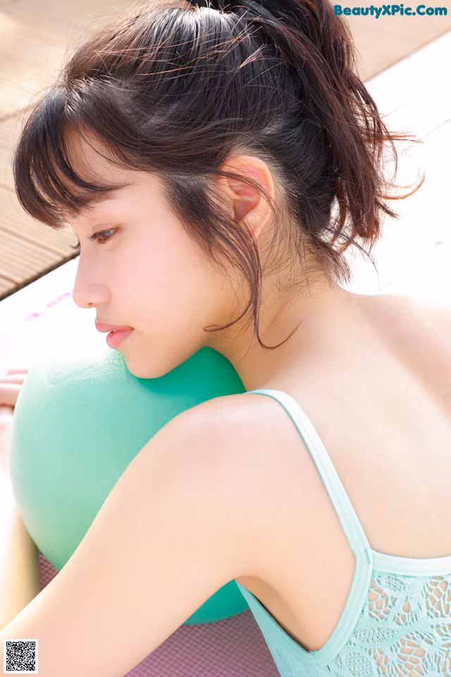 A woman in a green tank top sitting on a yoga mat.