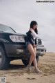 A woman standing next to a car in the desert.