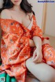 A woman in an orange kimono sitting on a bed.